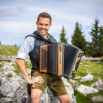 Richi Abenthung sitzt mit seiner Steirischen Harmonika auf einem Fels