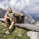 Stefan Kern sitzt mit seiner Steirischen Harmonika auf einer Bank